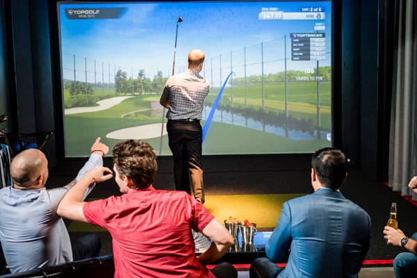 Man plays golf in Topgolf Swing Suite while others watch